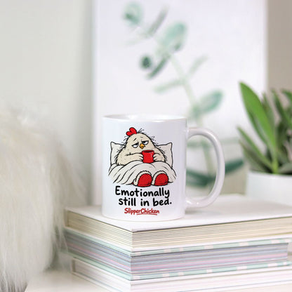 White Sleepy Mug with a chicken tucked into bed, Emotionally still in bed quote, and red SlipperChicken logo